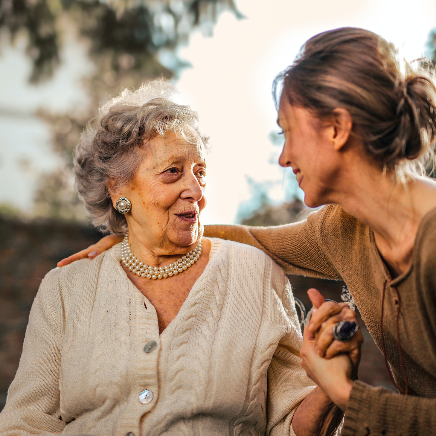 A young woman wraps her arms around an elderly woman sitting down
